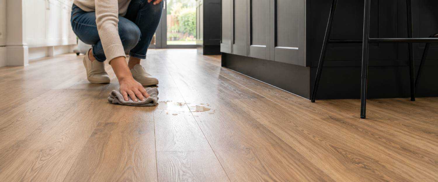 Person wiping a small spill from modern wood effect vinyl flooring beside a kitchen island in a bright contemporary kitchen