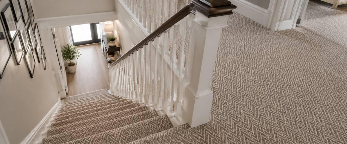 Contemporary staircase and landing with a neutral herringbone carpet, white spindles, dark oak handrail and bright natural light