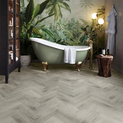 Mint-green freestanding clawfoot tub with brass feet and a white towel, in a tropical plant mural bathroom with a herringbone wood floor.