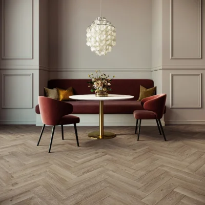 Elegant dining area with a round marble table on a gold pedestal, burgundy chairs and banquette, floral centrepiece, shell chandelier, and herringbone floor.