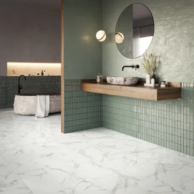 Contemporary bathroom with sage-green tiled walls, a floating wooden vanity with a stone basin and wall faucet, round mirror, pendant lights, plant and marble floor.
