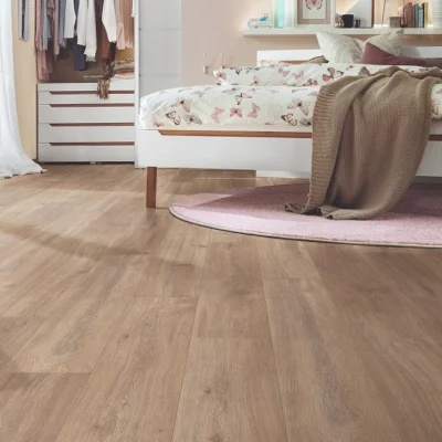 Bright bedroom featuring a white bed with butterfly-printed duvet, a pink circular rug, a brown knit throw, and a wardrobe with hanging clothes along a wooden floor.