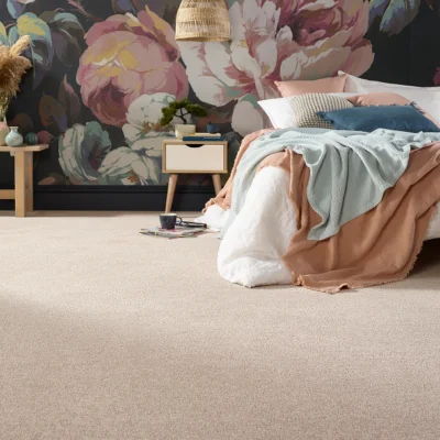 Cozy bedroom with a dark floral wallpaper, a bed with peach and mint throws, white bedding, a woven pendant light, and a small side table with plants.