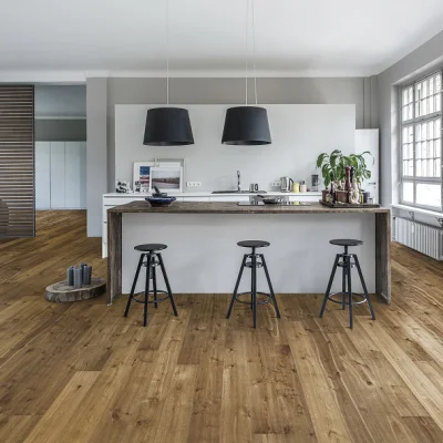 Bright open-plan kitchen with a wooden island and white base, three black bar stools, two black pendant lights, large window and a plant on the counter.