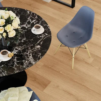 Top-down view of a round black marble table with a vase of white roses, two coffees and a pastry, beside a blue-grey chair on a light wooden floor.