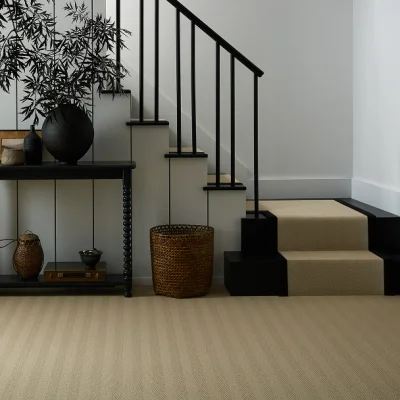 Modern interior with a beige carpet staircase, black metal railing, and a console table topped with a large black vase and woven baskets by the wall.