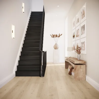 Bright entryway with a dark staircase on the left, light wooden floor, a console table with lamp and a vase of dried flowers, wall art.
