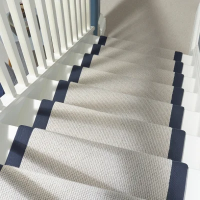An overhead view of a carpeted staircase with beige steps and dark navy edge trim, white balustrade on the left and a blue wall at the top.