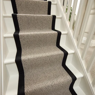 Interior staircase with a beige patterned carpet runner bordered in black on both sides, white balustrades and walls.