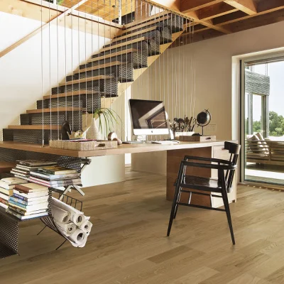 Bright home office under a floating staircase with a thick wooden desk, iMac, plants, books and rolled plans; large glass door to a sunny patio.