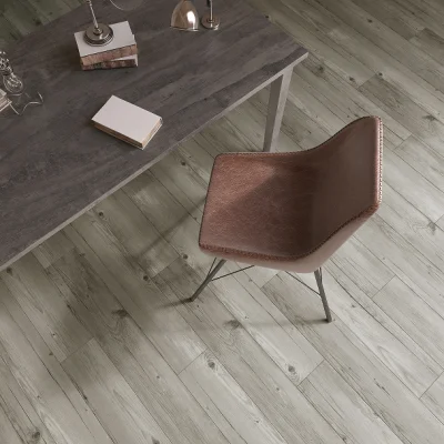 Top-down view of a grey wooden desk with a small stack of books and a lamp, paired with a brown leather chair on light wood flooring.