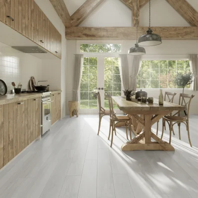Bright rustic kitchen with wooden beams, a large wooden dining table and chairs, white floors, and glass doors to a garden; natural light streams in.