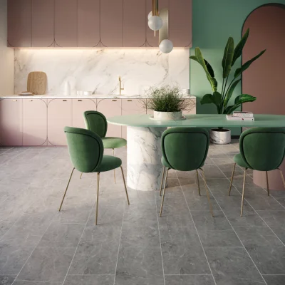 Pastel pink kitchen with marble backsplash, a round green dining table, green velvet chairs with gold legs, a tall leafy plant, and globe lights.