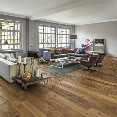 Bright living room with large grid windows, a grey L-shaped sofa with colourful cushions, brown swivel chairs, a white coffee table on a blue rug, and art prints.