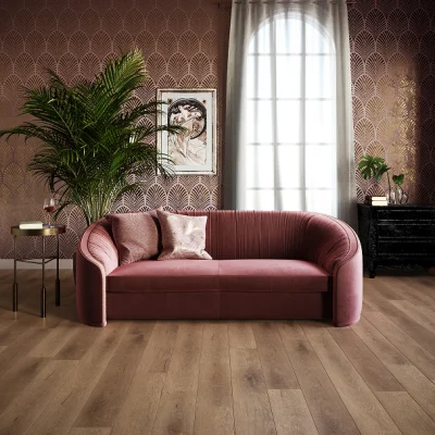 Pink velvet curved sofa in a stylish living room with patterned wallpaper, tall plant, framed art, window with sheer curtains, and a black sideboard.