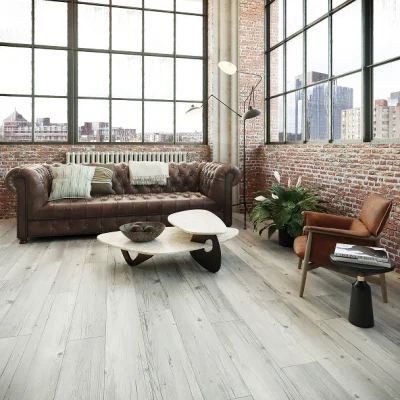 Industrial living room with exposed brick walls and windows; brown leather tufted sofa, circular marble-topped tables, armchair, plant and floor lamp.