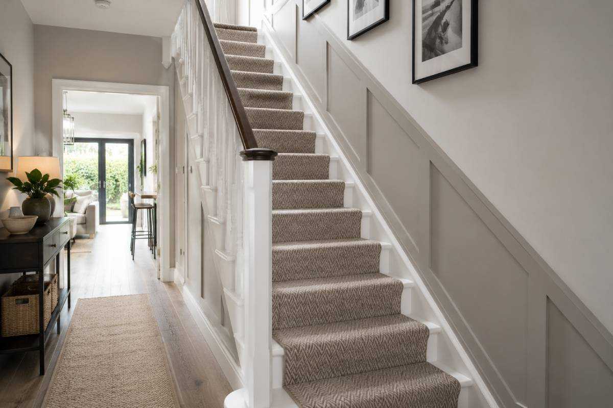 Contemporary staircase with a neutral herringbone patterned carpet, bright hallway, natural daylight and framed artwork along the staircase wall