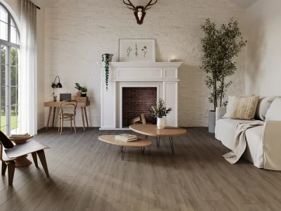 Bright living room with white brick fireplace and mantel, a deer head above, round coffee tables, cream sofa, and a tall plant by an arched window.