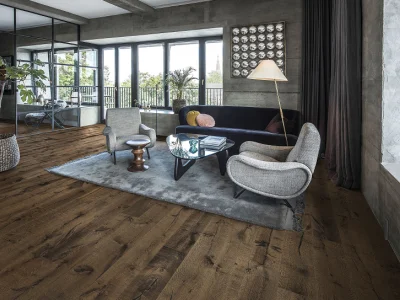 Modern living room with wood floors, windows and balcony; dark blue sofa, two chairs, glass coffee table on a rug, floor lamp and plants.