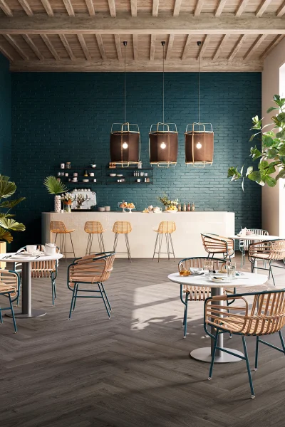 Modern cafe interior: teal brick wall, wooden beam ceiling, three pendant lamps, white counter with stools, round tables with rattan chairs, plants.