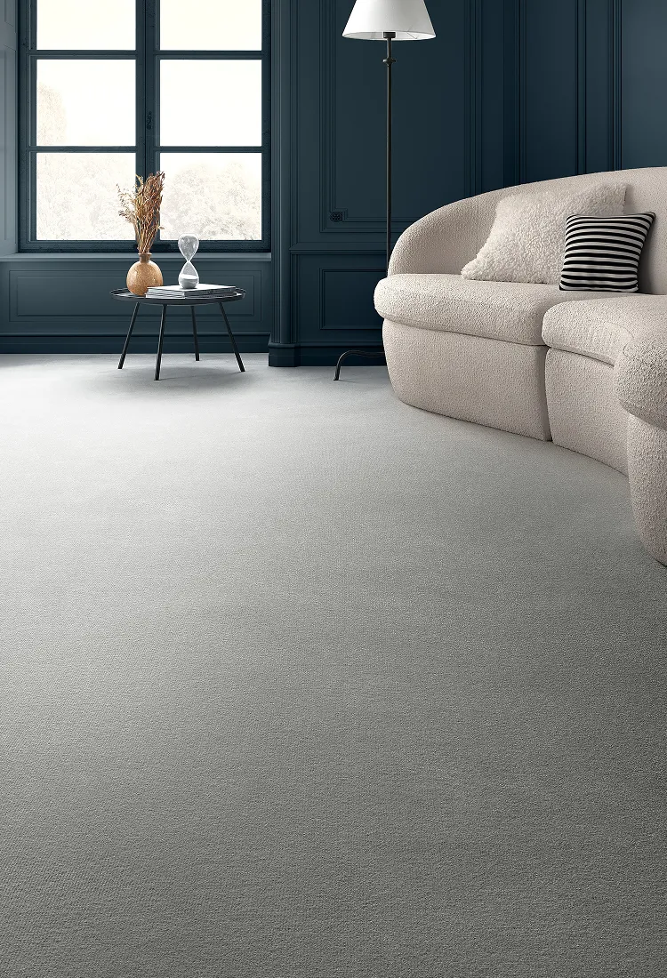 Modern living room with dark blue panelled walls, a beige sofa, striped cushion, tall floor lamp, and a side table with vase and hourglass by window.