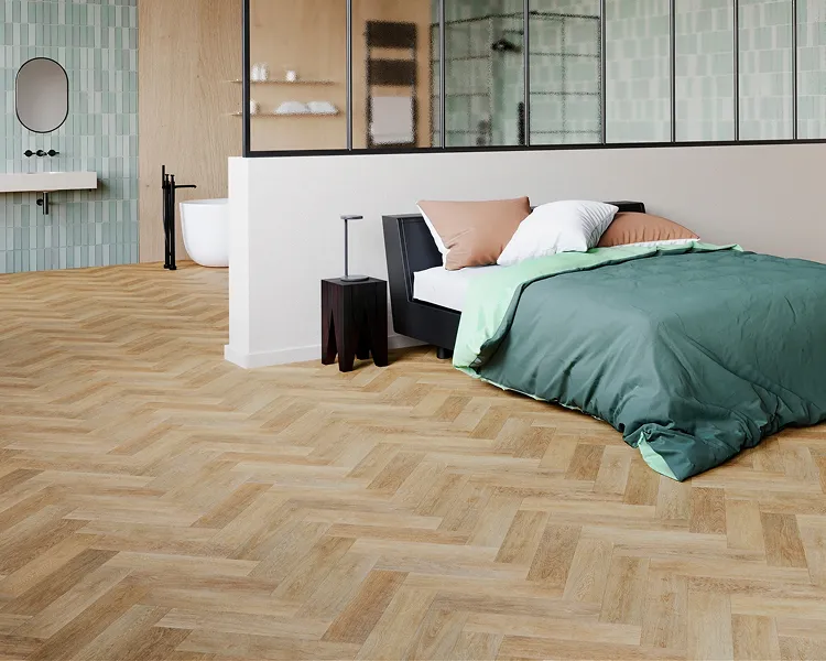 Modern room with a green duvet on a bed, beige and white pillows, black bedside tables, light wood herringbone floor; glass partition to mint-tiled bathroom.