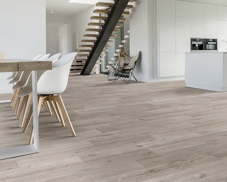 Open-plan kitchen and dining area with light wood flooring, white dining chairs along a wooden table, a black metal staircase, and a butterfly chair.