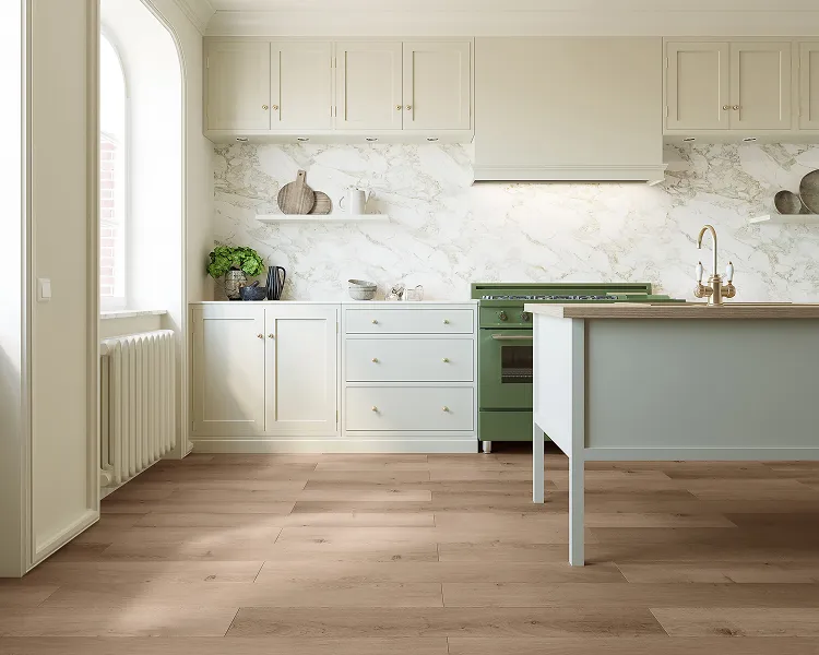 Bright kitchen with cream cabinets, marble backsplash, and a green range. A light blue island, wooden floor, copper faucet, and a window with radiator.
