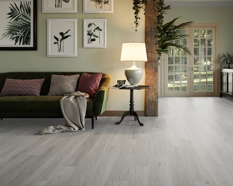 Living room with a green velvet sofa, decorative cushions and a beige throw; botanical art on the wall, a lamp on a side table, hanging plants, and French doors.
