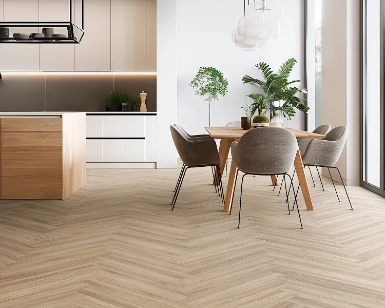 Bright open-plan kitchen and dining area with a herringbone wood floor, white and wood cabinets, a central island, and a wooden table with four grey chairs, with plants by the window.