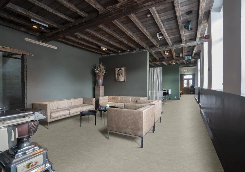 Industrial-style lounge with beige sectional sofas, exposed wooden beams, dark green walls, black coffee tables, and a tall vase of dried flowers.