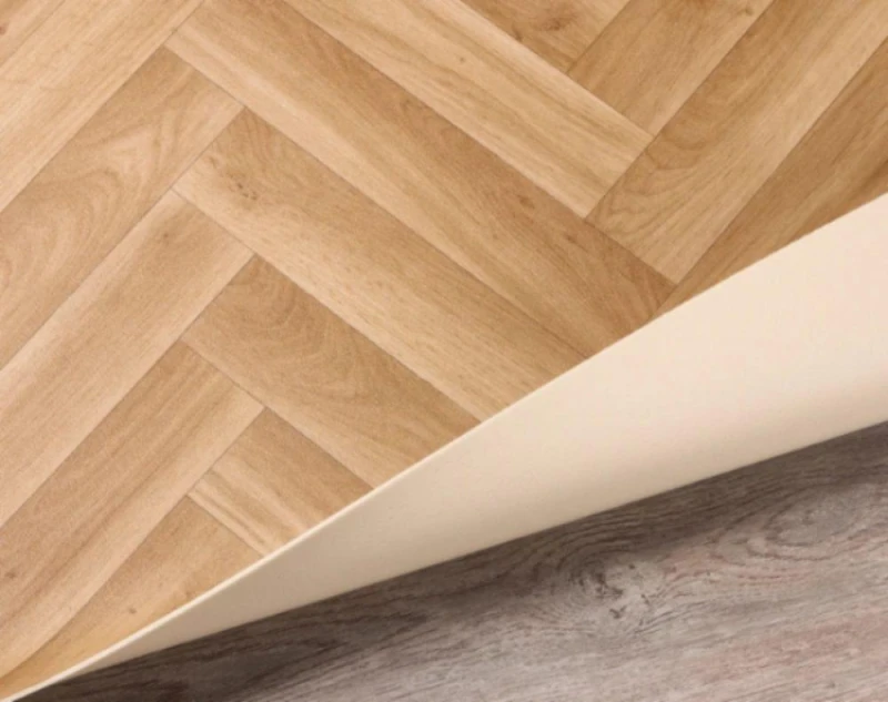 Light herringbone parquet floor with a white skirting board along a diagonal seam, adjoining a darker wood floor.