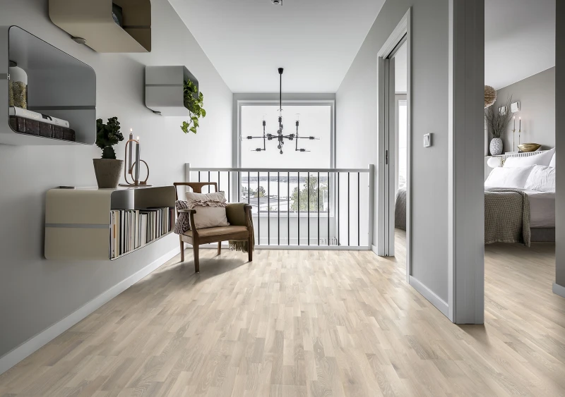 Bright grey landing with light wood floor, wall shelves, a brown armchair and potted plants; large window with a modern chandelier and harbour view, doorway to a bedroom on the right.