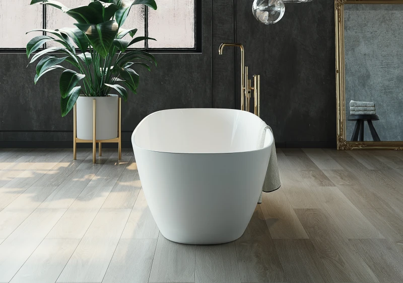 White freestanding bathtub with a gold faucet in a luxe bathroom, alongside a tall green plant in a white-and-gold planter and a gilded mirror.