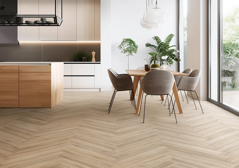 Bright open-plan kitchen and dining area with light wood herringbone flooring, white cabinets, a wooden island, grey chairs, and windows with plants.