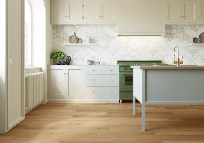 Bright cream kitchen with a marble backsplash, cream cabinets, and a green vintage oven. White island with a wooden top, brass faucet, and light wood flooring.